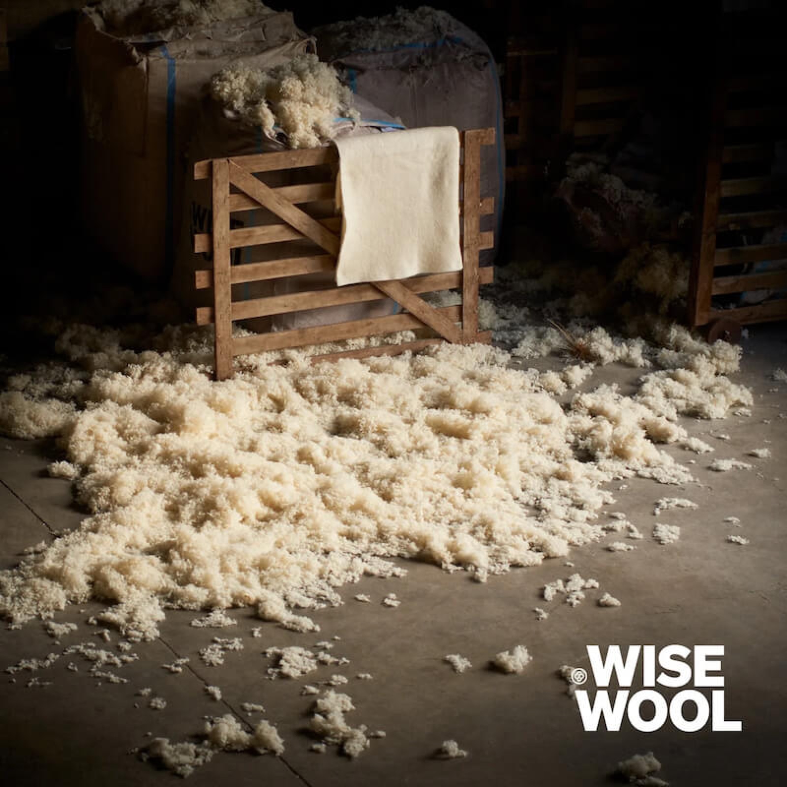 Raw engineered wool fibre from Wisewool, piled beside a folded felted blanket in a barn